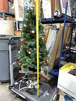 Full view of 4 ft artificial Christmas tree on wheeled cart including urn base and tape measure for scale