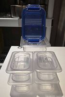 Stacked clear food pans with lids and blue-lidded produce keeper displayed