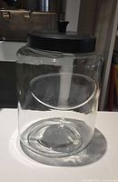 Tall cylindrical clear glass jar with black lid