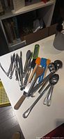 Assorted utensils spread on counter including tongs, ladles, spatulas, thermometer, knife, peeler