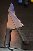 Two stainless chef knives with black handles on dark surface