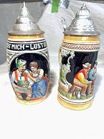 Front view of both beer steins showing relief scenes and pewter lids