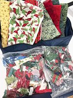 Overview of folded Christmas fabrics in blue carrier and two bags of scraps