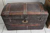Closed domed travel trunk showing exterior wood slats, embossed panels and hardware