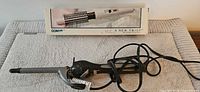 Revlon curling iron coiled on towel beside boxed Conair curling brush