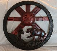 Full view of circular wood carving showing sun face, bear and human figure
