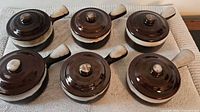 Six handled stoneware soup bowls with lids displayed on towel