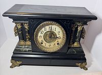 Front angled view of black Ingraham mantel clock showing columns, dial, and brass feet