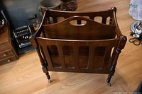 Walnut magazine stand side view showing slatted panels, turned legs, brass casters