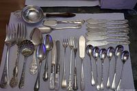 Entire lot laid out showing 27 pieces of silver plate flatware and serving utensils