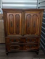 Front view of dresser showing paneled doors, four drawers, hardware, feet