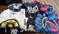 Folded garments showing Yankees top, Ecko shirt, Bruins jersey, mesh jersey, and camo hoodie