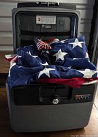 Open SentrySafe chest containing folded large American flag and small stick flags