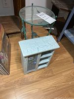 Round glass top metal vine side table beside painted cabinet