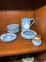 Group showing mug, six small plates, ashtrays and lighter on wooden shelf