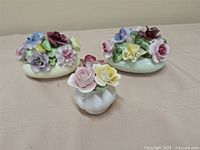 Three bone china floral figurines on cloth backdrop