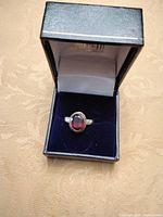 Front view of oval red garnet sterling silver ring in box
