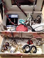 Open jewelry box showing assorted necklaces, pendants, earrings and rings in upper compartment
