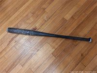 Full view of black metal baseball bat on hardwood floor