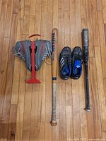 Full lot showing ski boots on carrier, two bats and batting shoes laid on wooden floor