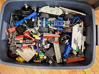 Overview of tote filled with assorted LEGO pieces including wheels, beams, plates and hull section