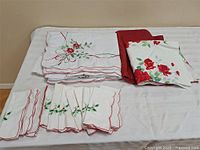 All linens folded on bed showing three distinct designs: poinsettia cloth, rose print cloth, holly napkins