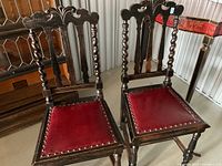 Front view of both carved wood chairs showing matching design and red seats
