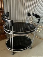 Full view of two-tier glass and metal table, shows frame, shelves, and handles