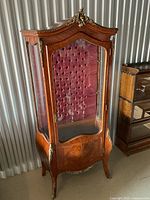 Full view of curio cabinet showing glass door, curved sides, red tufted back