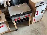 Wooden grill cart with silver lid and red knobs next to other play units