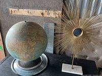 Globe on metal stand and sunburst sculpture side by side