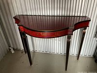 Front view of demilune hall table showing red chinoiserie apron, black legs