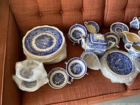 Group view of stacked plates, soup bowls, pitchers and bubble-wrapped bowls on sofa
