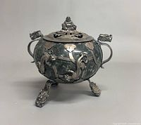 Front view of stone and silver tripod censer with lid, handles, and dragon feet visible