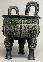 Full view of bronze tripod vessel showing decoration and handles