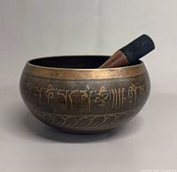 Singing bowl side view with mallet resting inside showing exterior script and border