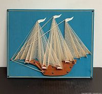 Full view of framed sailboat string art on turquoise board