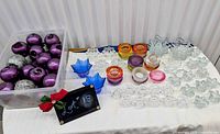 Wide view showing tub of metallic ball candles and assorted glass candle holders on table