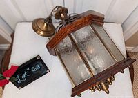 Overall view of lantern lying on cushioning showing hexagonal wood frame, brass trim, etched glass panels, chain and ceiling canopy
