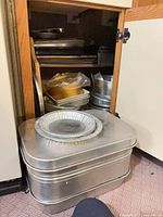 Cabinet showing stacked pans, roaster on floor, variety of bakeware visible
