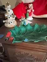 Overview showing ceramic Christmas tree, elf figurine and holly candy dish on furniture top
