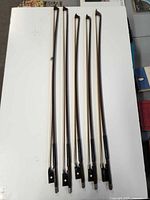 Five Glasser violin bows standing upright showing frogs and tips
