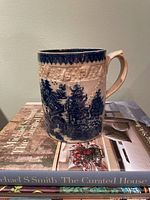 Full view of blue transferware mug on books showing pattern and handle