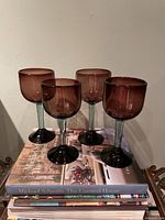 Four amethyst coloured wine glasses standing on books, front view