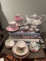 Group shot showing most pieces including white floral teapot, blue and white cups, pink lusterware cups and saucers, floral sugar bowl, assorted teacups