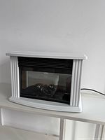 Front view of white mini electric fireplace heater on shelf