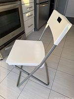 side view of folded-open white IKEA folding chair showing seat, backrest, frame