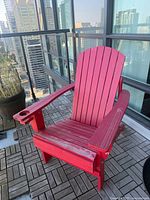 Front view of red Adirondack chair on balcony, showing cup holder and slatted design