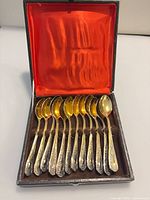 Open case showing all 12 gold-tone teaspoons in red satin-lined interior