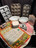 Overall view of all items in lot including bakeware, bowls, dishes, espresso set, tea towel, apron and soap